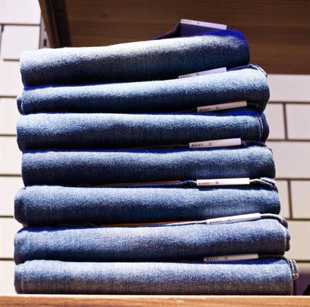 Stacked of folded jeans in store on wooden shelf.の写真素材
