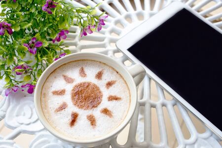 latte art coffee with sun design in white cup and white mobile on white vintage tableの写真素材