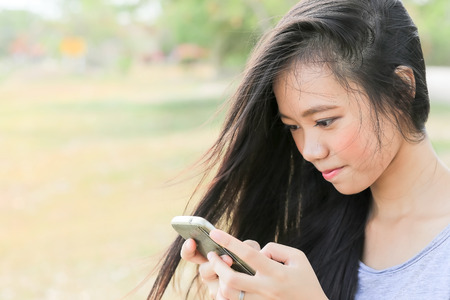 close up young Asian woman sitting in garden using a mobile telephoneの写真素材