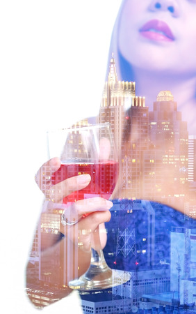 double exposure and de-focused , woman hand in blue dress holding red wine in wineglass with midnight townscape backgroundの写真素材