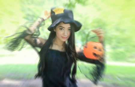 de-focused and selective sharpen at one eye , portrait of Asian woman on black dress and holding plastic pumpkin doll in garden , Halloween conceptの写真素材