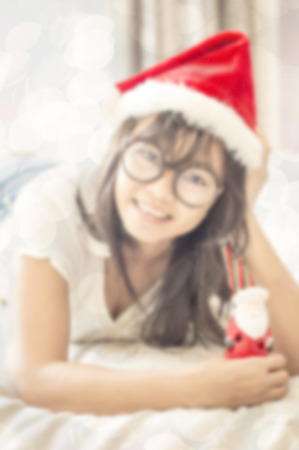 de-focused , close up asian woman dressed in white clothes holding  toy of Santa in hand , lay down on white bed , double exposure with bokeh lightの写真素材