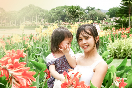 Standing mother holding her daughter in garden posing for the cameraの写真素材