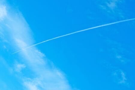 Trace of an airoplane on a cloudy blue skyの写真素材