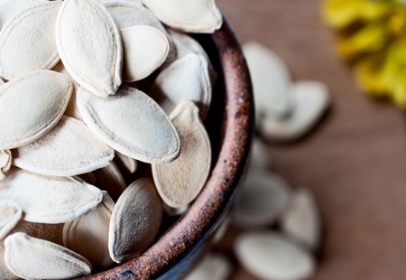 Ceramic bowl full of pumpkin seeds on wooden board backgroundの写真素材