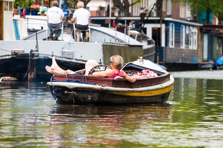 AMSTERDAM, JUNE 10: Motorboat with resting man on Amsterdam canal on June 10, 2011. Amsterdam has been called the "Venice of the North" for its more than one hundred kilometers of canals, about 90 islands and 1,500 bridges.のeditorial素材