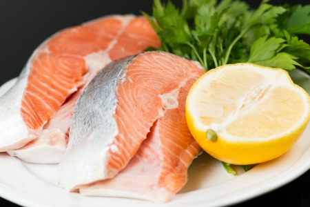 Raw trout steak with parsley and lemon on plateの写真素材
