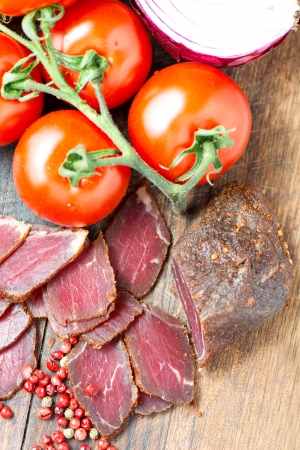 Prosciutto slices, pepper corn and tomatoes on wooden tableの写真素材