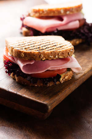 Sandwich with ham, salad, tomato on wooden cutting boardの写真素材