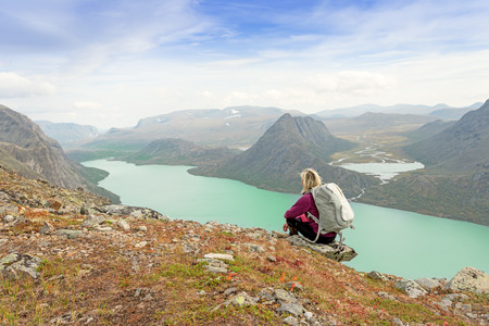 Hiker with backpack relaxing on cliff of a mountain and enjoying valley and lake view at Jotunheimen National Park, Norwayの写真素材
