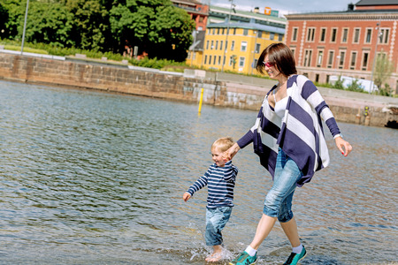 Little preschool boy playing on shore outdoors with brunette motherの写真素材