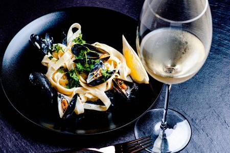 Blue mussels and pasta in black plate on stone surfaceの写真素材