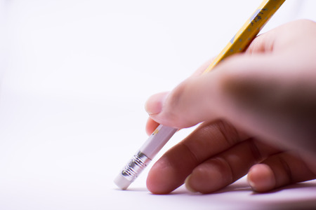 A woman's hand is erasing something with the rubber sticking with the pencil on the white background. There are the plain background on the left side which should be used as background or a card.の写真素材