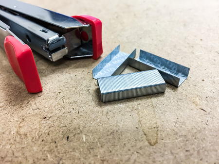 Pink stapler and staples are on the brown table. This is the tool for stapler, it is a kind of the stationery in office or school. There are the empty space on the bottom side which could be added a text or somethingの写真素材