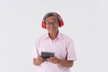 white studio portrait of senior asia retired elderly man wear red headphone listening music from tabletの写真素材