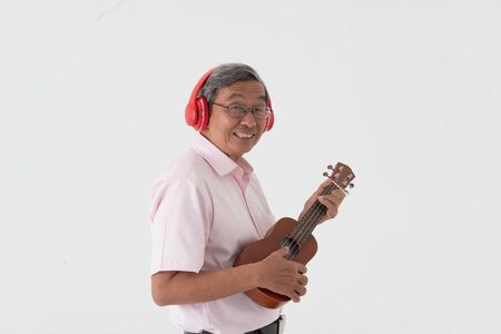 white studio portrait of senior asia retired elderly man wear red headphone and playing ukuleleの写真素材