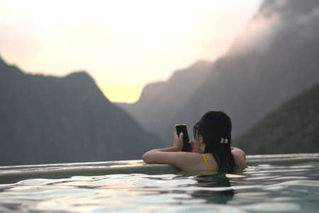 Woman inside a pool consulting the cell phoneの写真素材