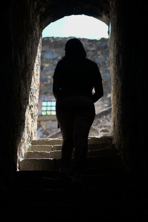 Silhouette of a woman climbing stairs through a tunnel towards the light from outside
