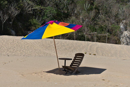 Wooden chair on the beach with a table and umbrella next to itの写真素材
