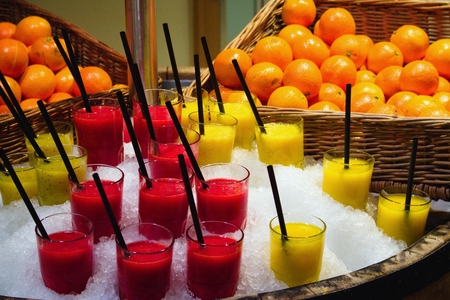 Glass cups of fresh fruit smoothies with drinking straws displayed in a pile of ice in the store