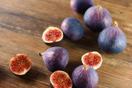 Ripe blue and purple figs, both whole and cut in half, randomly spilled on dark wood tableの写真素材