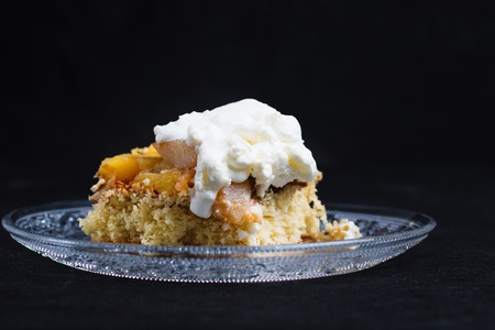 Side view of sponge apple cake with whipped cream on glass plate on solid black background