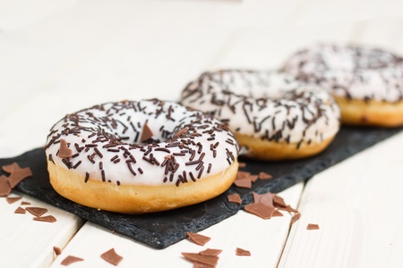Three white donuts with chocolate sprinkles on black slate stone serving trayの写真素材
