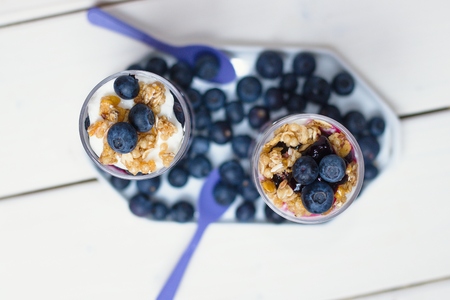 Top down view on two blueberry yogurt parfaits in tall glasses on white wooden tableの写真素材