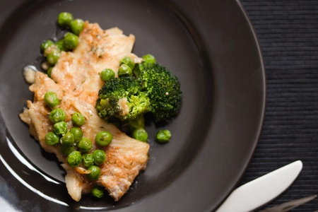 A serving of fried fish with peas and broccoli on black plate. Healthy low fat nutrient delicious dishの写真素材