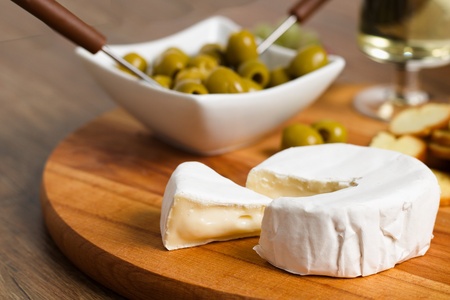 Camembert cheese on wooden board with roasted bread slices, olives and white wineの写真素材
