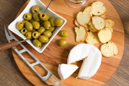 Top down view of soft cheese (camembert or brie) on wooden board with roasted bread slices and olives, Connoiseur party food, concept of quality luxury eatingの写真素材