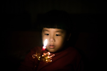 A boy ignite a candle in the darkness.の写真素材