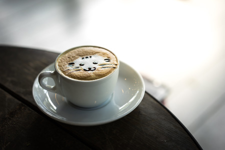 A cat face latte art coffee in white cup on wooden table in the morning.の写真素材