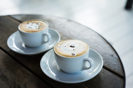A cat face and a bear face on latte art coffee in white cup on wooden table in the morning.の写真素材