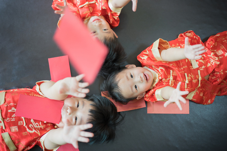 Happy chinese new year. 3 cute asian little boys are playing red envelopes together on the bed.の写真素材