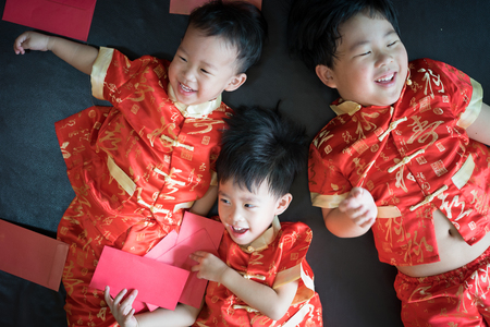 Happy chinese new year. 3 cute asian little boys are playing red envelopes together on the bed.の写真素材