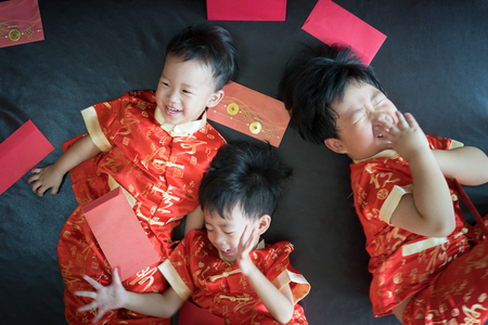 Happy chinese new year. 3 cute asian little boys are playing red envelopes together on the bed.の写真素材