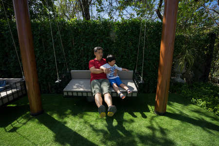 Grandpa and grandchildren are playing and talking on swings in the backyard.の写真素材