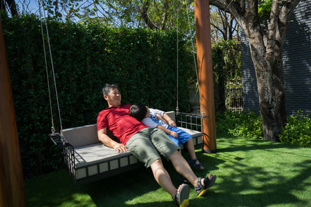 Grandpa and grandchildren are playing and talking on swings in the backyard.の写真素材