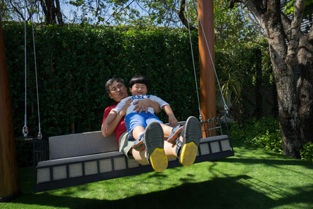 Grandpa and grandchildren are playing and talking on swings in the backyard.の写真素材