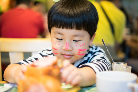 A painted face boy is eating delicious pork knuckle in a steak restaurant.の写真素材