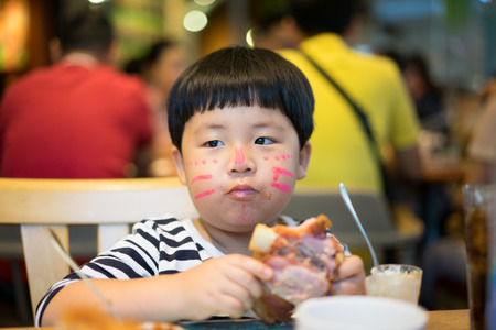 A painted face boy is eating delicious pork knuckle in a steak restaurant.の写真素材