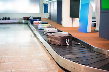 Many luggages are laying down on the conveyor belt at the airport. Baggage claim. White wall background.の写真素材