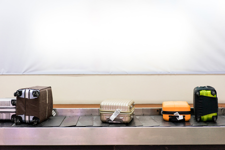 Many luggages are laying down on the conveyor belt at the airport. Baggage claim. White wall background.の写真素材