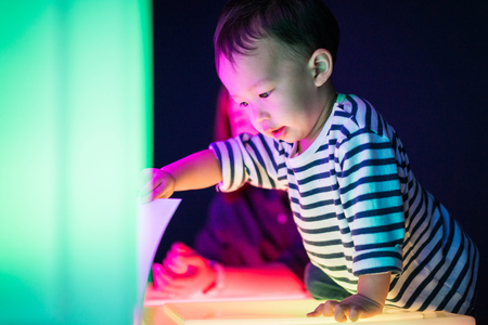 A boy and his mom are playing colorful light cubes together in the dark study room.の写真素材
