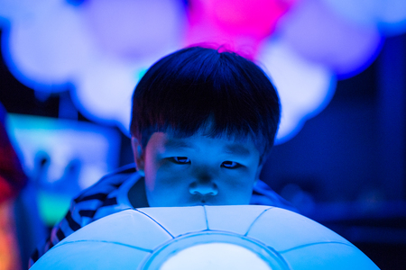 A boy is playing colorful light balls in the dark study room.の写真素材