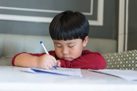 A Asian boy is drawing a picture in the topic of My family with a pen.の写真素材