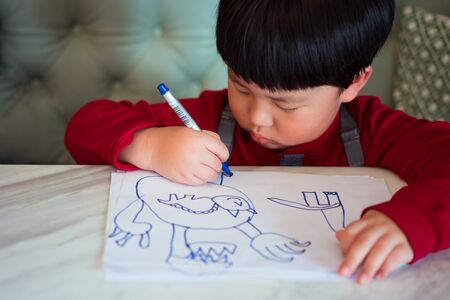 A Asian boy is drawing dinosaur on paper, in the topic of My pet with a pen.