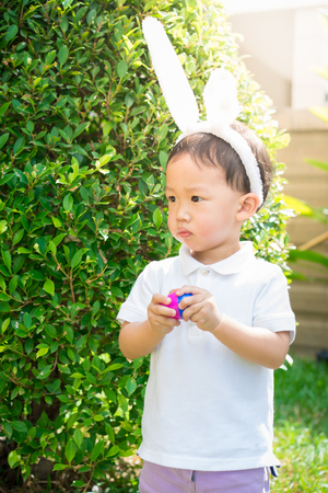 A cute asian little boy with bunny ears holding plasstic Easter egg in the garden.の写真素材