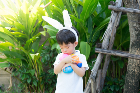 A cute asian little boy with bunny ears holding plasstic Easter egg in the garden.の写真素材